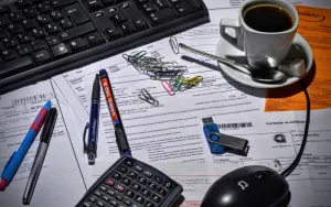 Accounting & Bookkeeping System Cup of tea, keyboard, mouse, biros, calculator on top of papers.